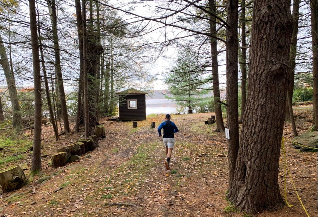 man jogging down a wooded trail with lake in background
