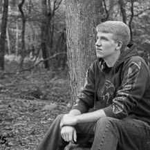 Black and white portrait of Jake Burkhardt sitting amongst trees